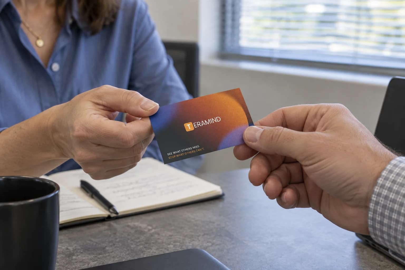 A Teramind business card exchanged across a meeting table.