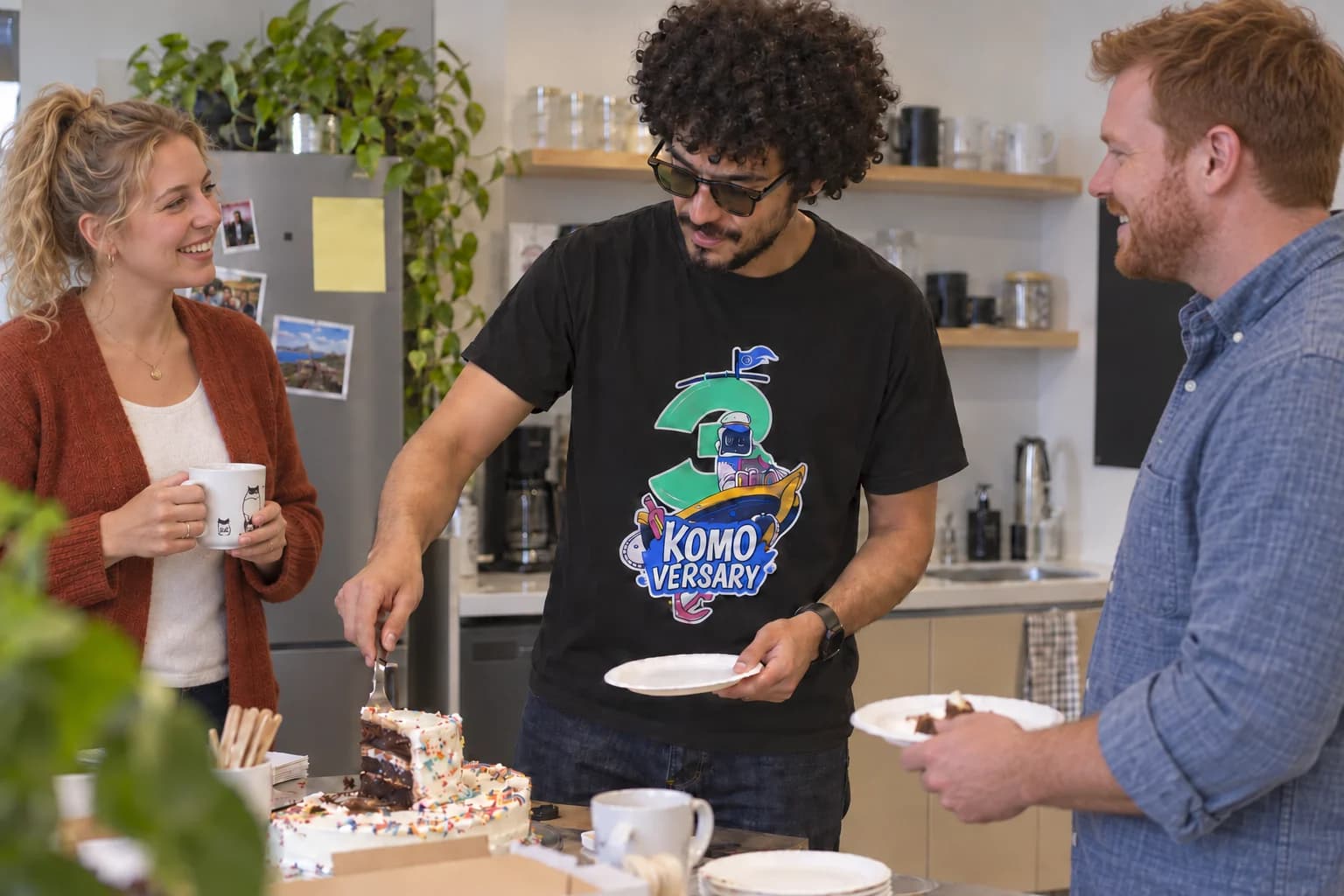 Coworkers of different ages sharing cake, with a Komodor anniversary shirt.