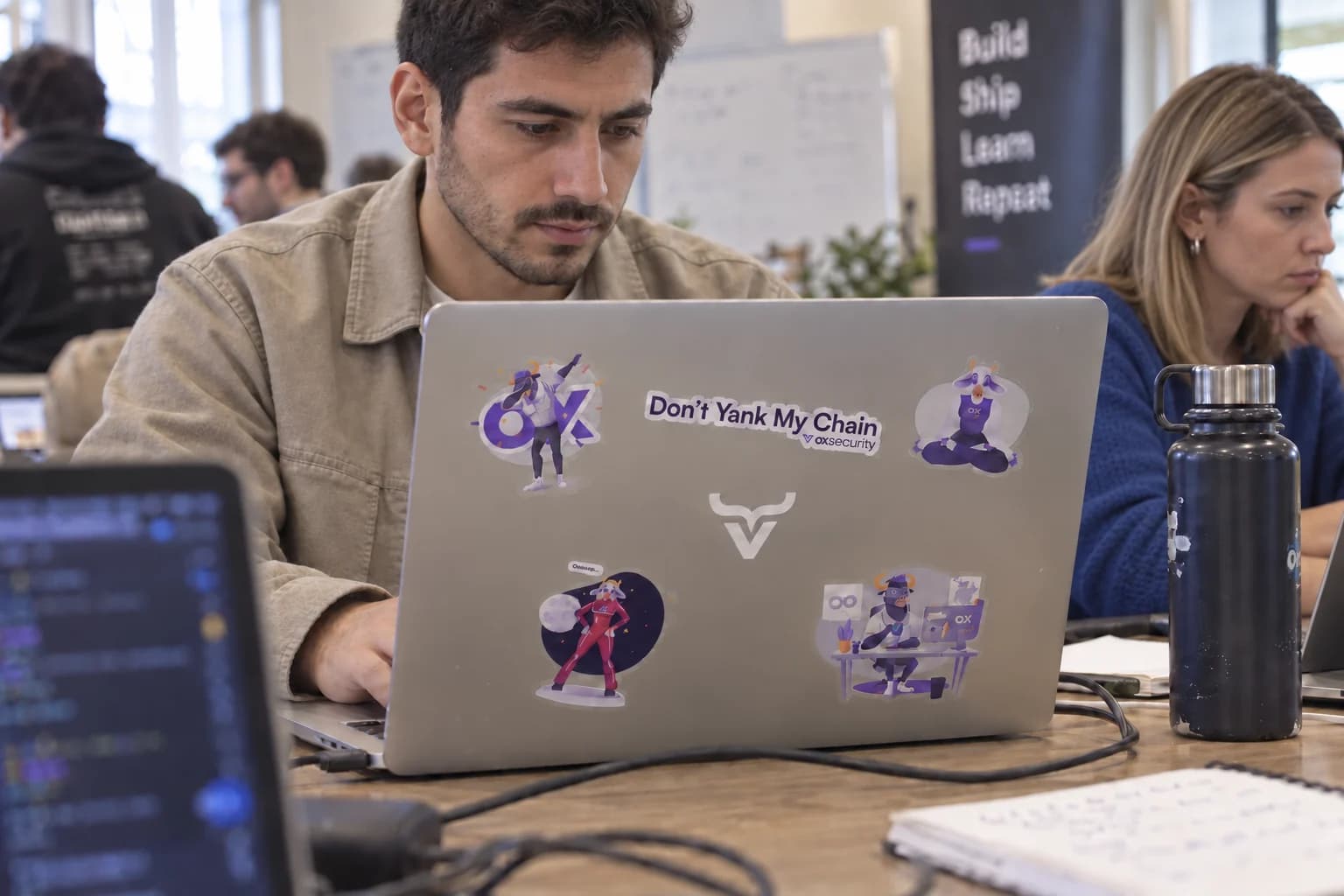 Different developers working with an OX Security sticker-covered laptop.