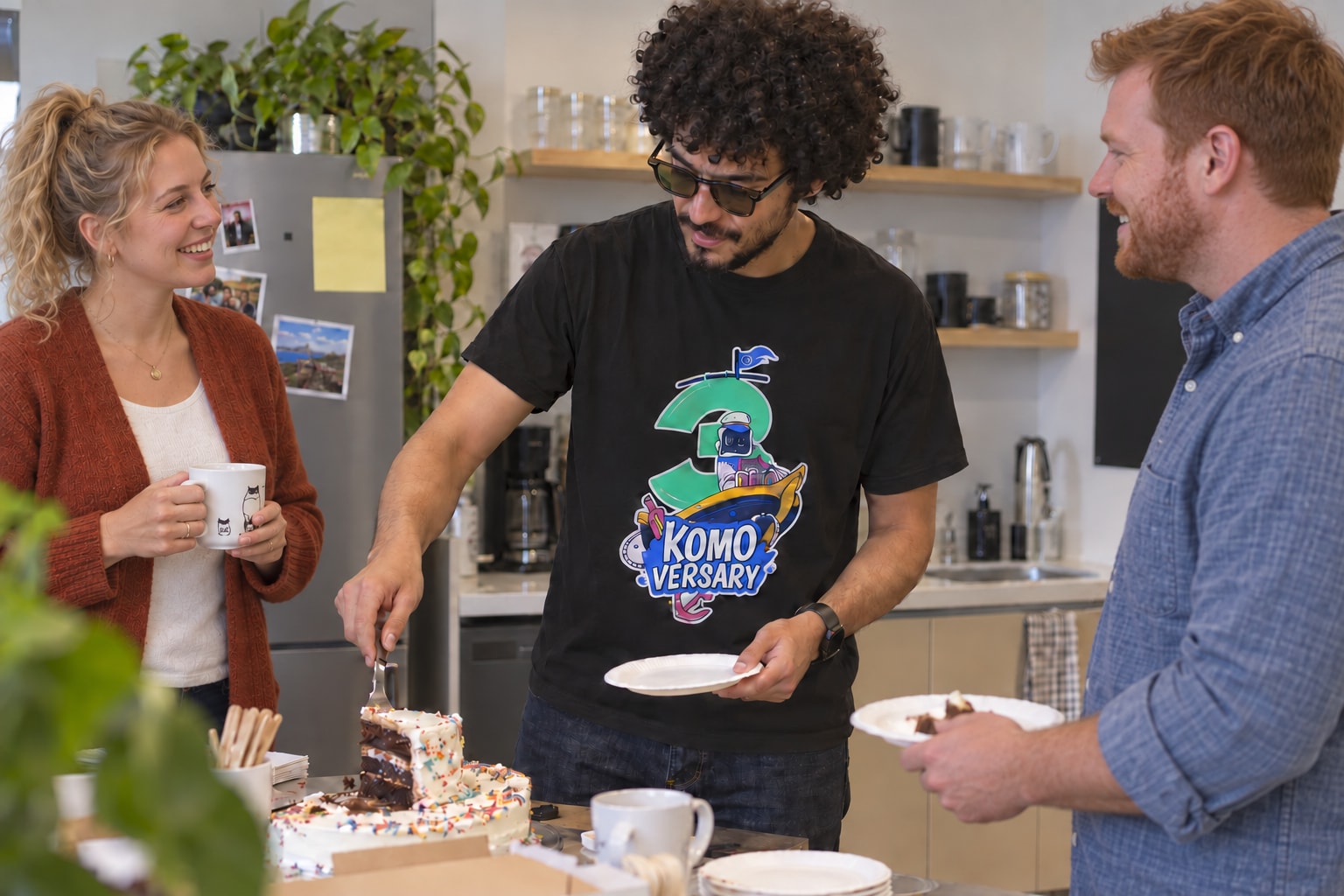 Coworkers of different ages sharing cake, with a Komodor anniversary shirt.