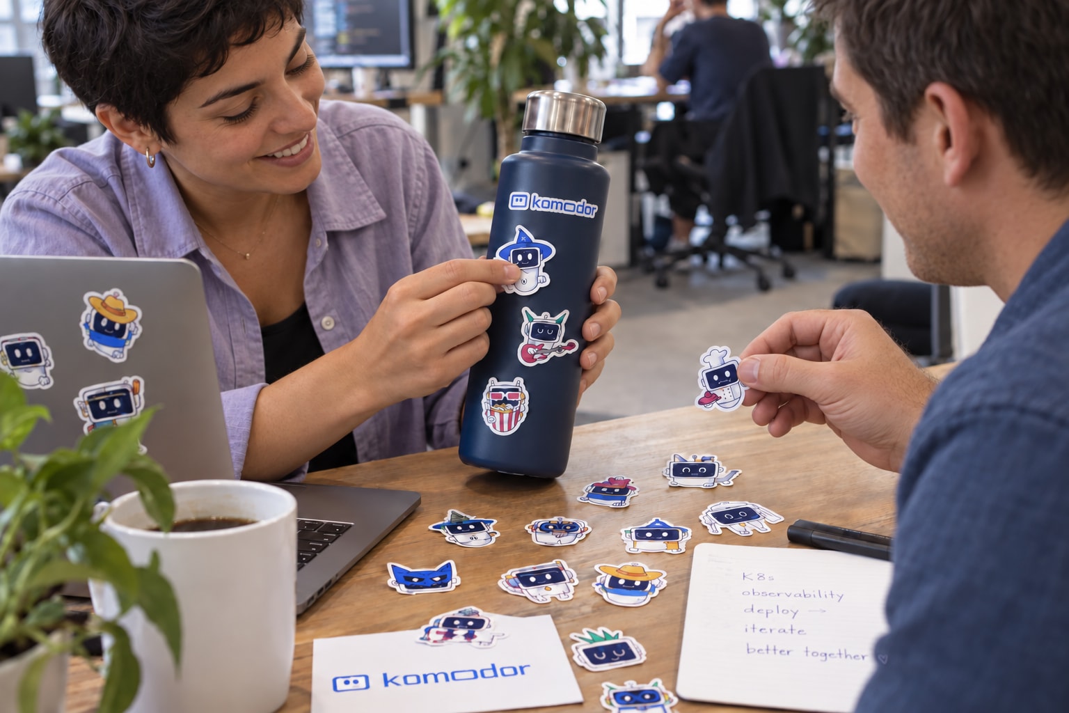Coworkers with distinct appearances applying Komodor stickers to a bottle.