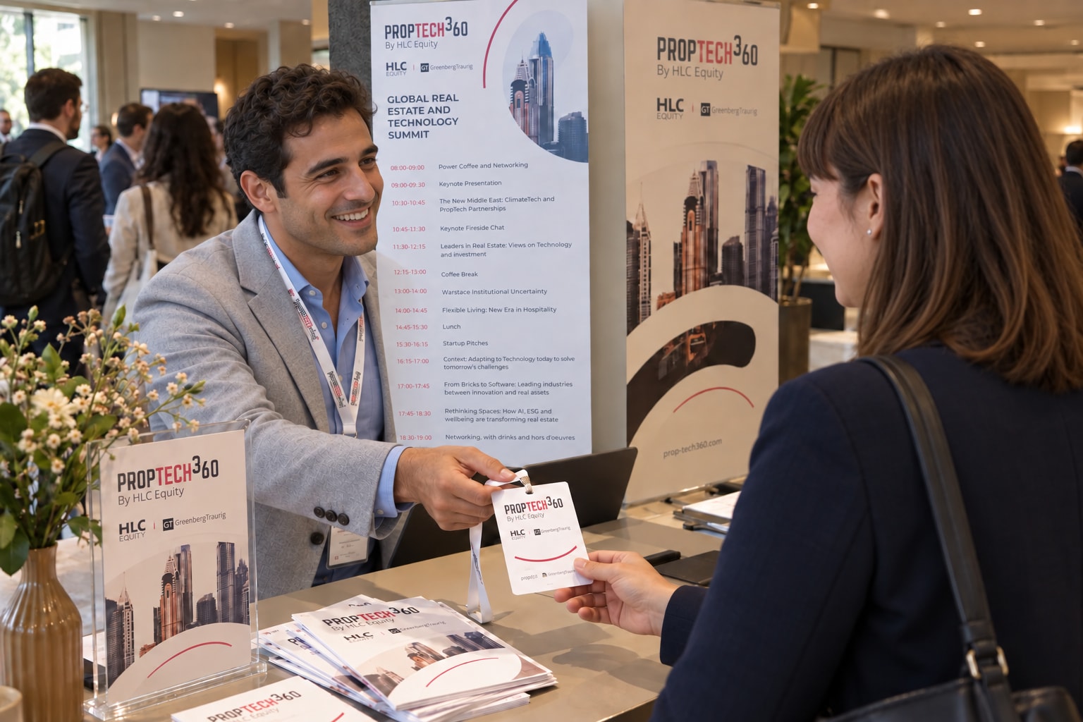 A conference coordinator handing a PropTech360 badge to an arriving attendee.