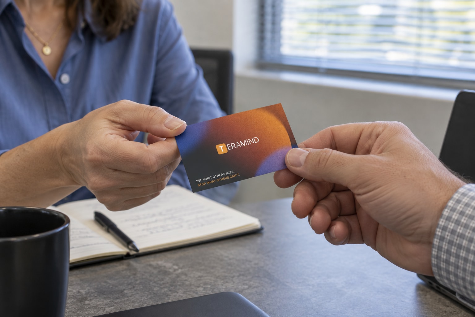 A Teramind business card exchanged across a meeting table.