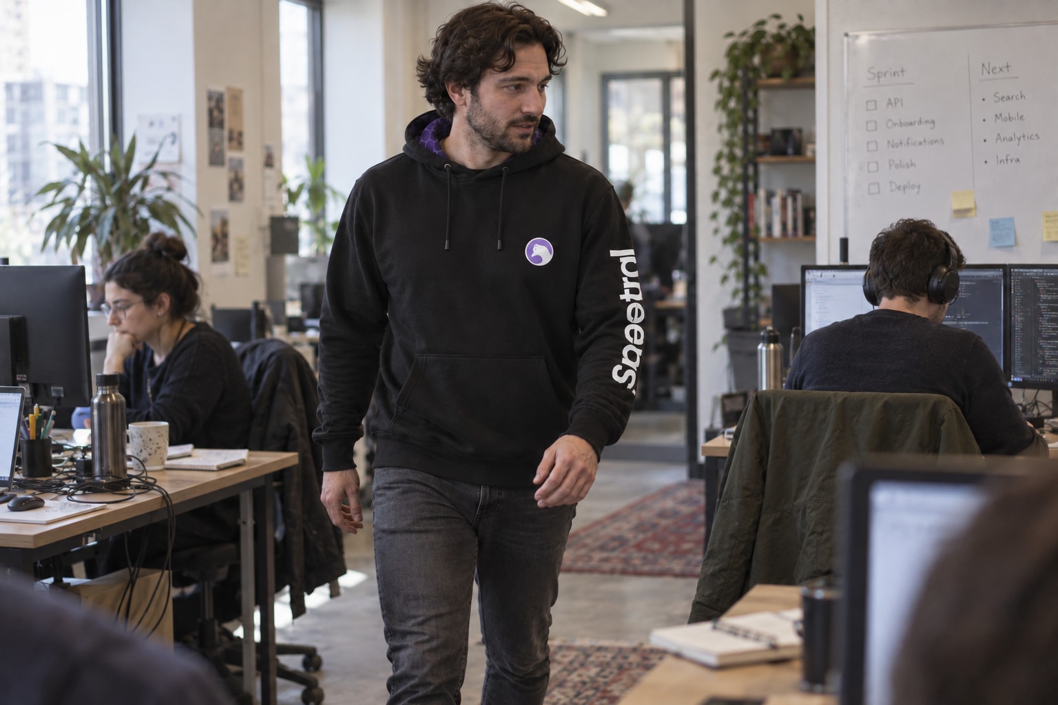 An engineer walking between shared office desks wearing the original black Spectral hoodie.
