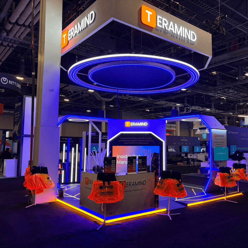 Teramind exhibition booth at a Las Vegas trade show - glowing blue light ring, branded counters and orange swag bags.